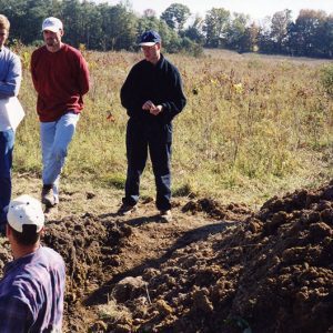 Land Judging. Man in trench. five men observing-Website