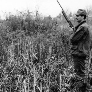 Man in field holding gun. Young person looks on .Photo by Robert Mills