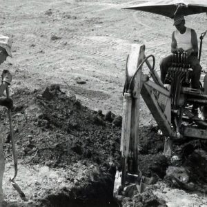 Man operating a digging machine while a man with shovel looks on. Photo by Robert Mills