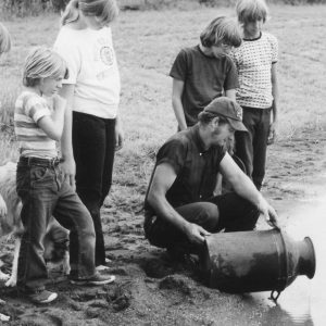 Man with bucket pouring something in pond as 5 kids look on .Photo by Robert Mills