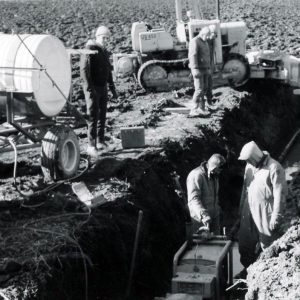 Two men in trench with machinery as two men look on. Lots of equipment standing around. Photo by Robert Mills