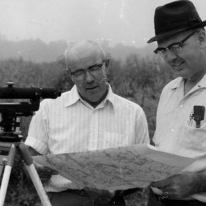 Two men standing by surveying instrument look at map .Photo by Robert Mills