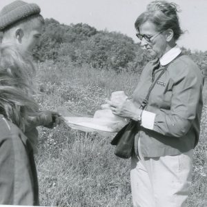 Two students look on as a woman displays a specimen in the field. Photo by Robert Mills