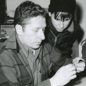 Two students look on as man holds bird in hand. Photo by Robert Mills