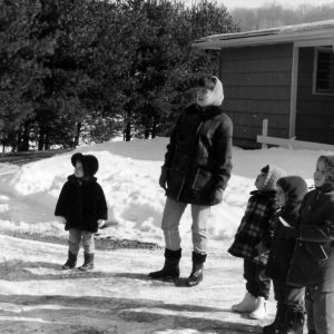 Woman and four children stand in snow looking off in distance .Photo by Robert Mills