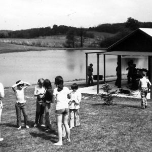 Woman and group of children beside pond and a shelter .Photo by Robert Mills