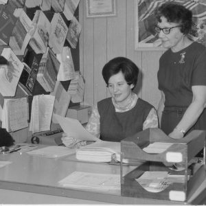Woman sitting at desk looking at a paper while a woman standing looks on-0001.Photo by Robert Mills