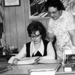 Women sitting looking at note book while another woman standing looks on.Photo by Robert Mills