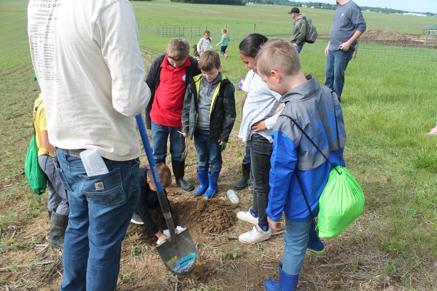 Students gathered around a hole they dug preparing to plant undies for the soil health experiment