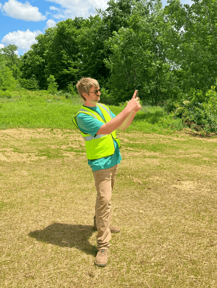 Sam Foley on a site inspection. He is wearing a high visibility vest and taking a photo of the site that was just seeded.