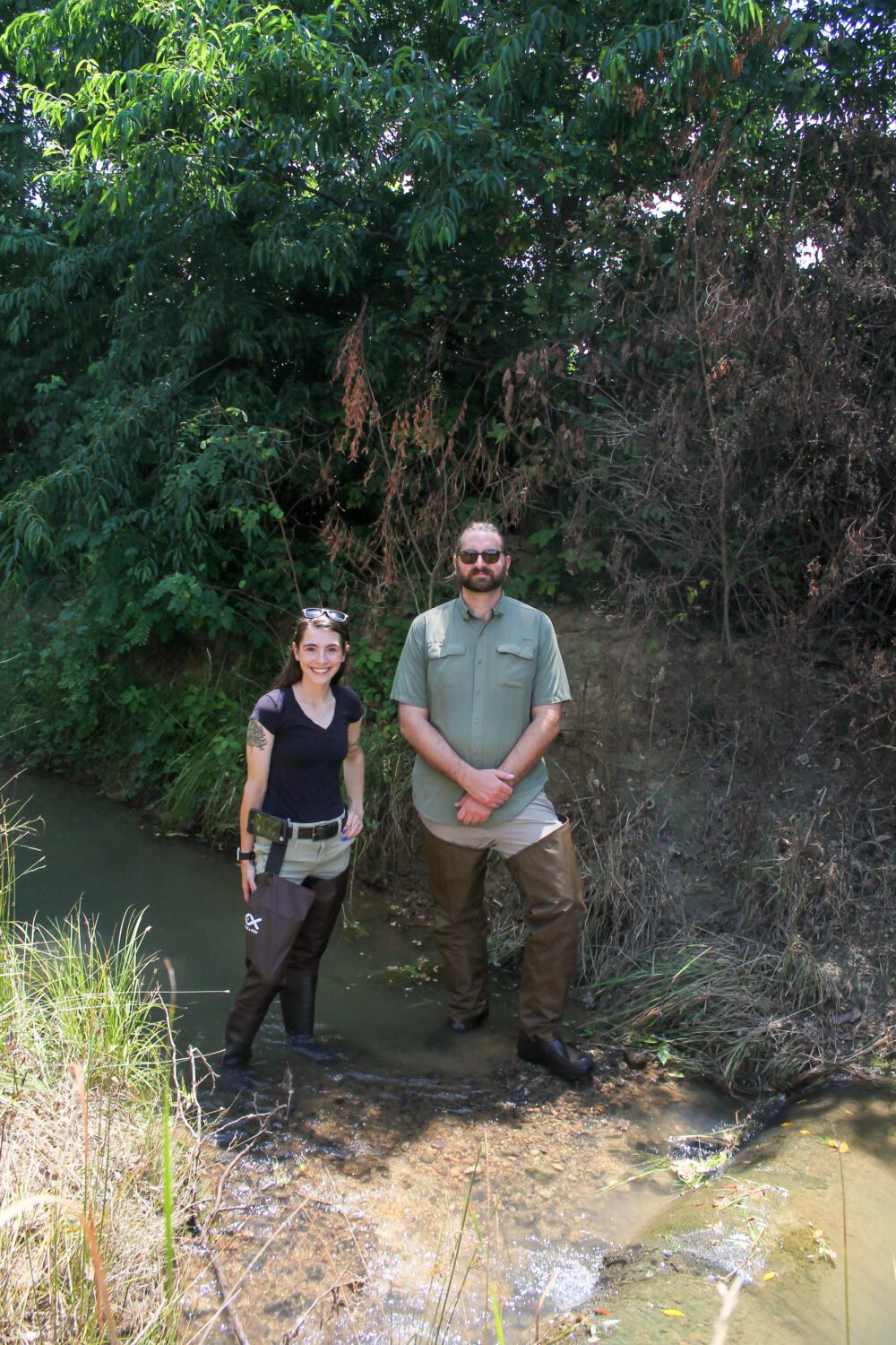 Two technicians in waders standing in a stream smiling at the camera. 