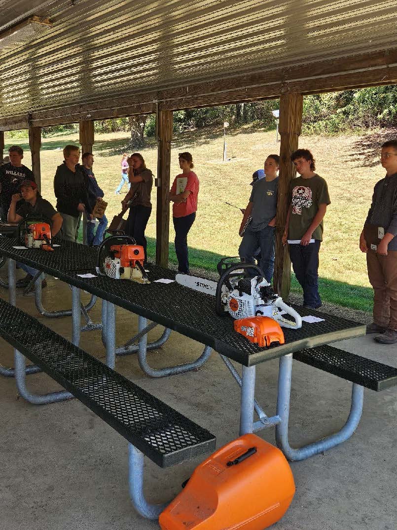Students gathered around a table under a pavilion at the chainsaw part identification table.