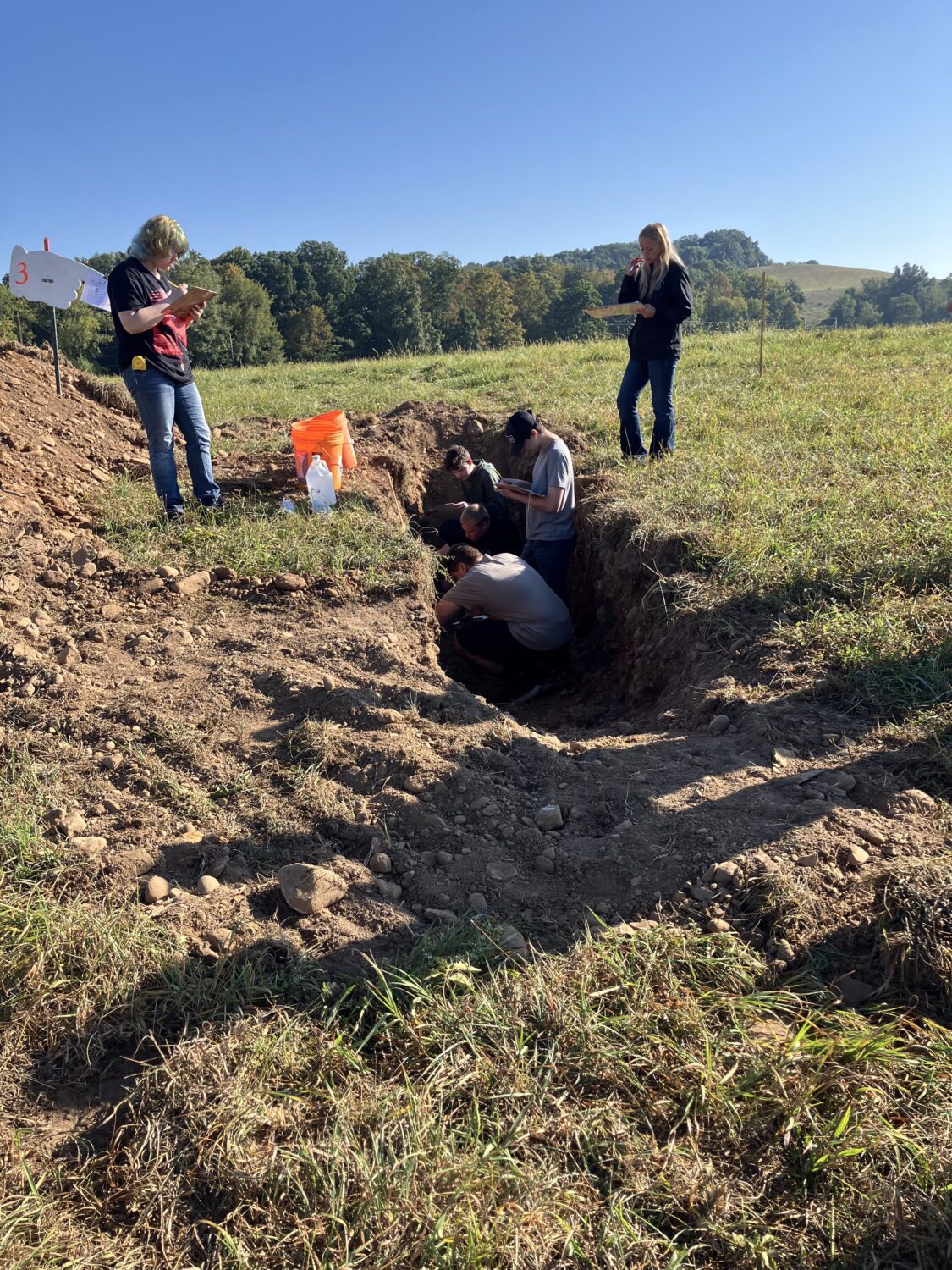 3 students standing in a soil pit. 2 students standing above the pit.