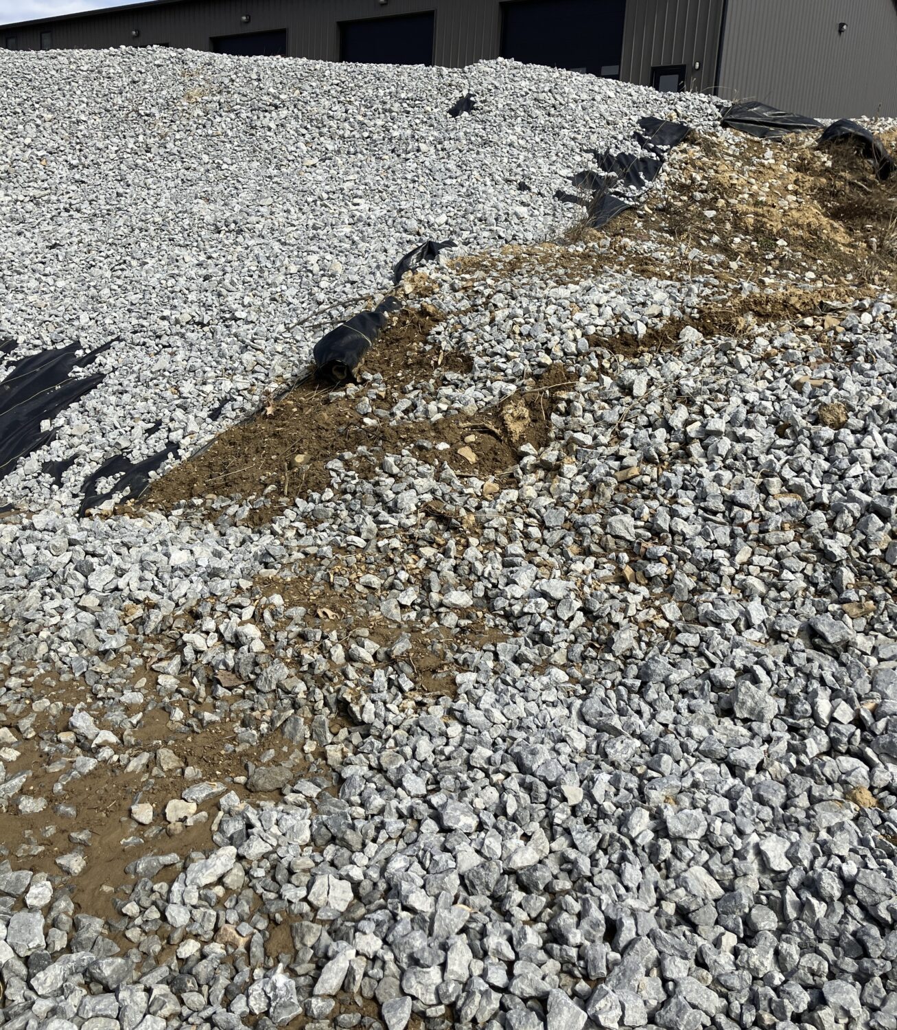 A hillside partially covered in riprap to stabilize it. There is geotextile matting down and some bare soil remaining.