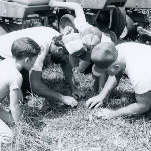 Three men and a boy examining soil in a farm field